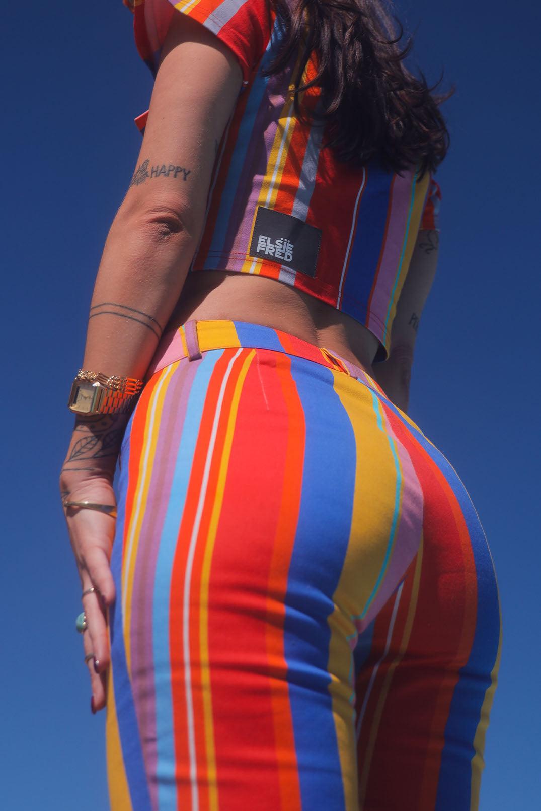 back view of girl in candy primary coloured horizontal striped trousers on blue sky background